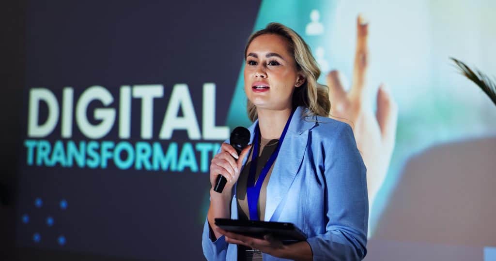 Stage, presentation and woman at seminar with microphone, tablet and speaker on digital transformation for business